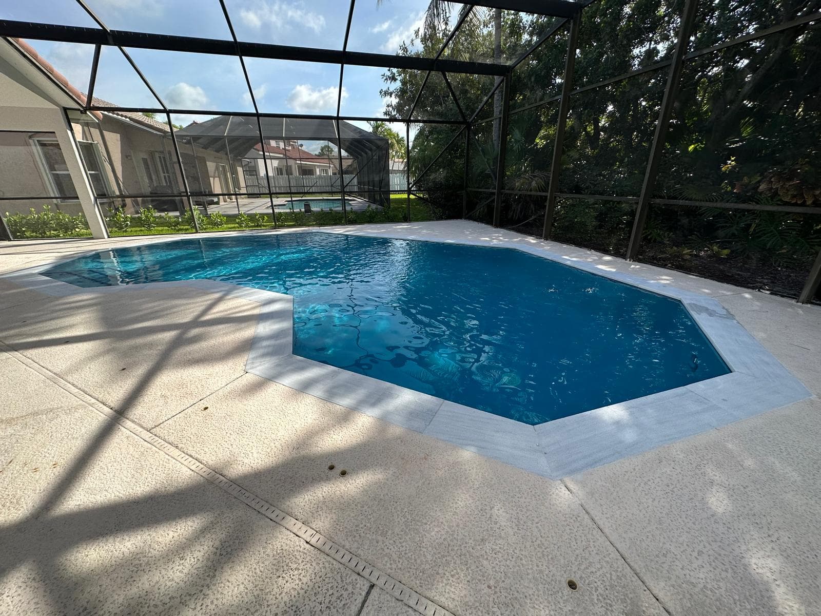 The same screened octagonal pool after remodeling, with new light grey coping, a fresh interior finish and clear blue water